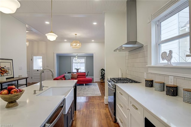 kitchen featuring backsplash, wood-type flooring, appliances with stainless steel finishes, wall chimney exhaust hood, and light countertops