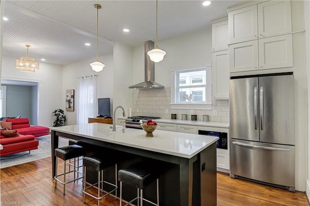 kitchen featuring tasteful backsplash, light wood finished floors, light countertops, appliances with stainless steel finishes, and wall chimney exhaust hood