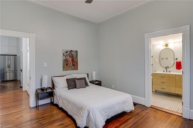 bedroom featuring baseboards, ensuite bath, hardwood / wood-style floors, and stainless steel refrigerator