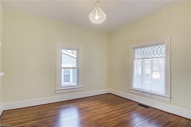 empty room with a notable chandelier, visible vents, dark wood-type flooring, and baseboards