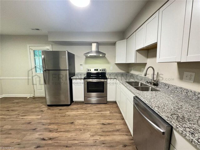 kitchen with white cabinetry, sink, stainless steel appliances, wall chimney range hood, and light wood-type flooring