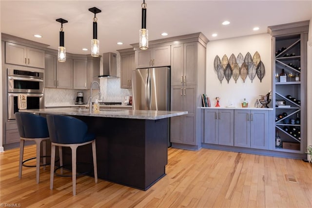4166 Lytchfield Ct, Winston-Salem, NC 27104 - kitchen featuring appliances with stainless steel finishes, wall chimney range hood, light stone countertops, a kitchen breakfast bar, and light wood-style flooring