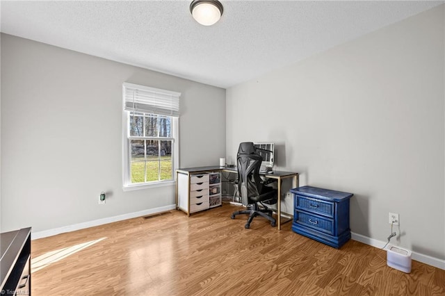 home office with a textured ceiling and light hardwood / wood-style flooring