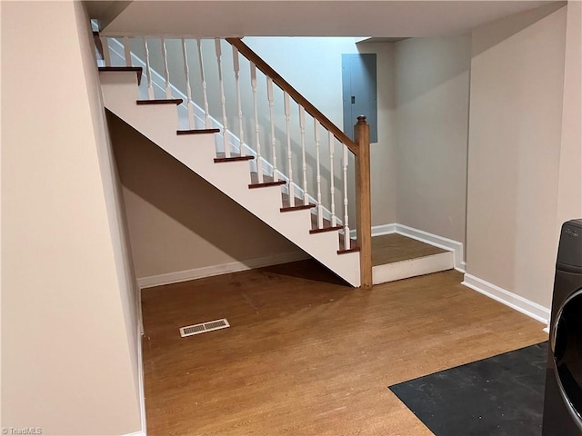 stairway with hardwood / wood-style floors and electric panel