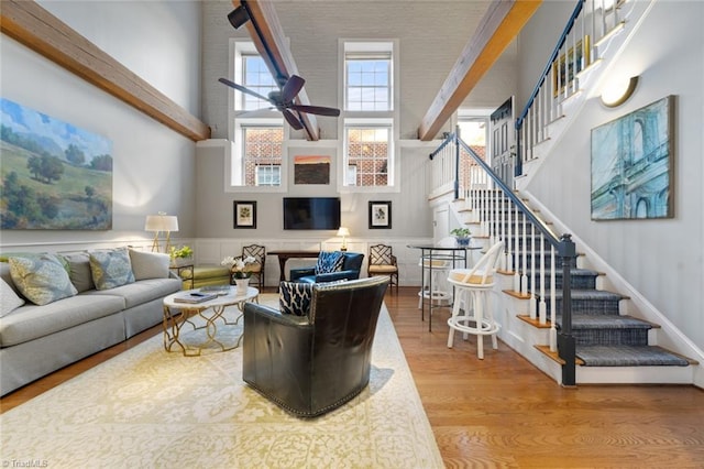 living room with a wainscoted wall, stairs, a towering ceiling, wood finished floors, and a ceiling fan