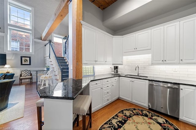 kitchen featuring a sink, stainless steel dishwasher, white cabinetry, light wood-style floors, and a peninsula