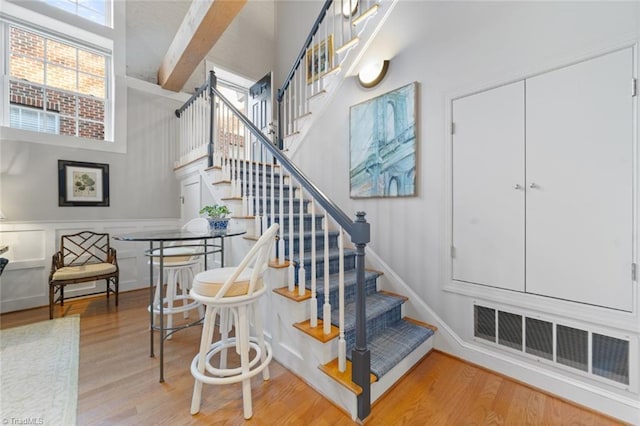 stairway with visible vents, beam ceiling, wood finished floors, a decorative wall, and a towering ceiling