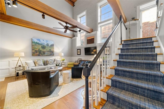 living area with a wainscoted wall, beamed ceiling, wood finished floors, stairway, and a towering ceiling