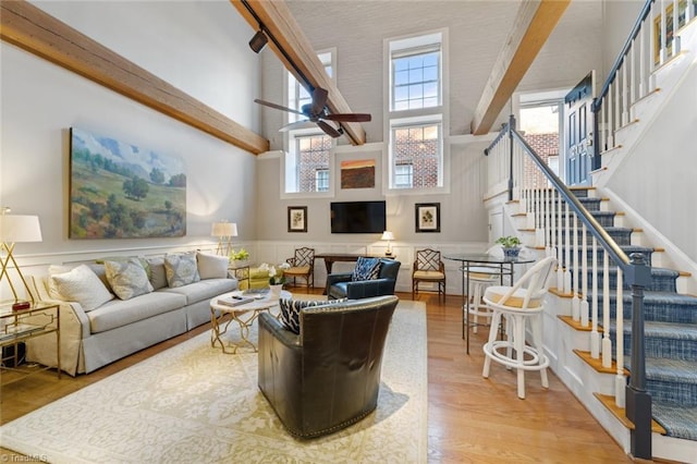 living room with a ceiling fan, wood finished floors, stairway, a high ceiling, and wainscoting