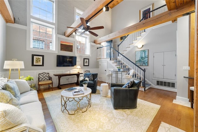 living room with wood finished floors, a wainscoted wall, visible vents, stairs, and a towering ceiling