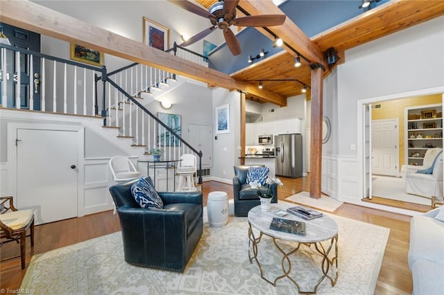 living area featuring stairs, beam ceiling, light wood-style flooring, rail lighting, and a decorative wall