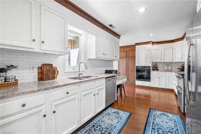 kitchen featuring visible vents, stainless steel appliances, wood finished floors, white cabinetry, and a sink