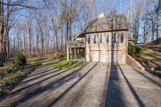 view of front of property featuring stucco siding, a deck, aphalt driveway, a garage, and a chimney