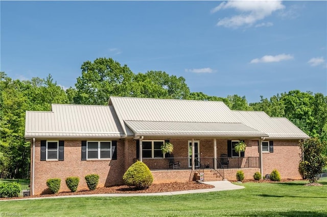 view of front facade featuring covered porch, brick siding, a front yard, and a standing seam roof