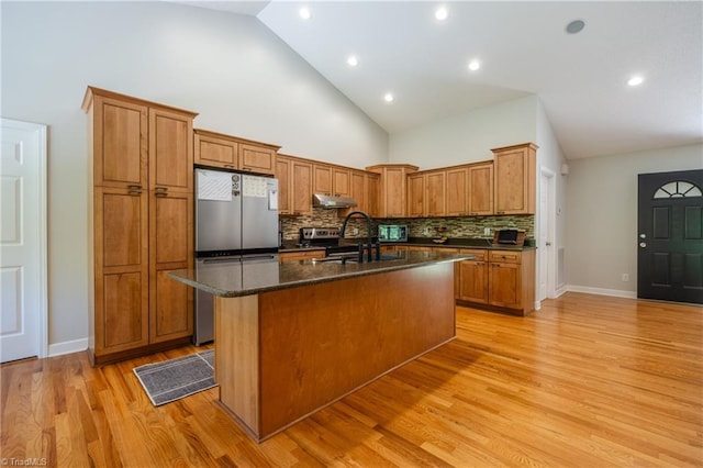 kitchen featuring under cabinet range hood, an island with sink, a sink, decorative backsplash, and appliances with stainless steel finishes