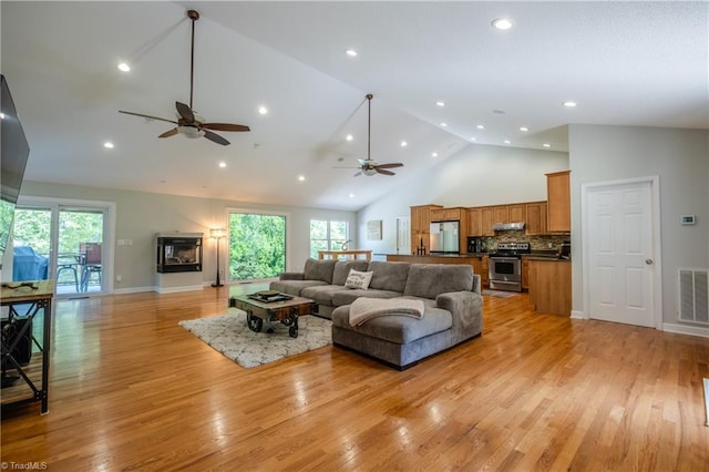 living room with a wealth of natural light, light wood-type flooring, ceiling fan, and high vaulted ceiling