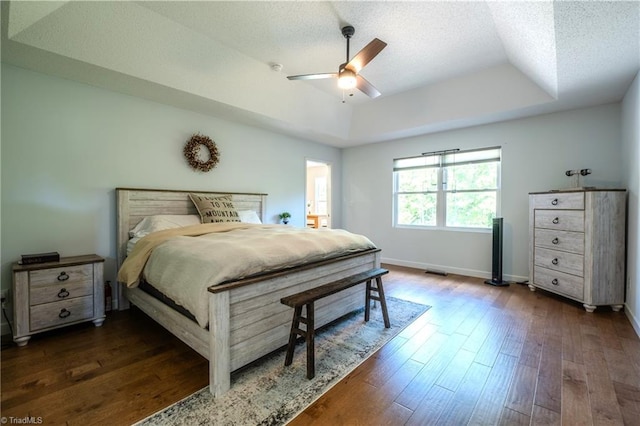 bedroom with baseboards, a raised ceiling, dark wood finished floors, and a ceiling fan