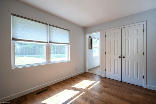 unfurnished bedroom with multiple windows, a textured ceiling, visible vents, and wood finished floors