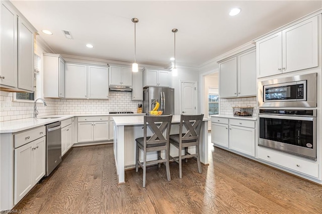 7722 NW Meadows Dr, Stokesdale, NC 27357 - kitchen featuring appliances with stainless steel finishes, tasteful backsplash, under cabinet range hood, dark wood-style flooring, and ornamental molding