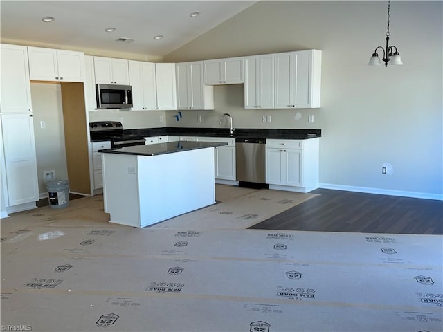 kitchen featuring lofted ceiling, stainless steel appliances, white cabinets, hanging light fixtures, and dark countertops