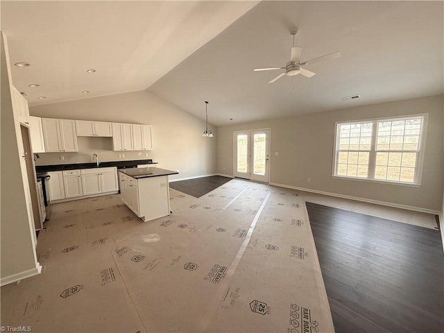 kitchen featuring pendant lighting, dark countertops, open floor plan, white cabinetry, and a kitchen island