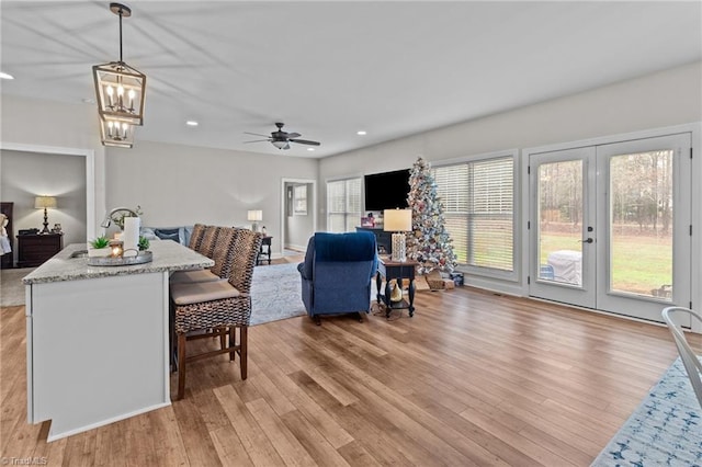 living room with ceiling fan with notable chandelier, french doors, a wealth of natural light, and light hardwood / wood-style flooring