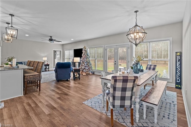 dining room with ceiling fan with notable chandelier, wood-type flooring, and french doors