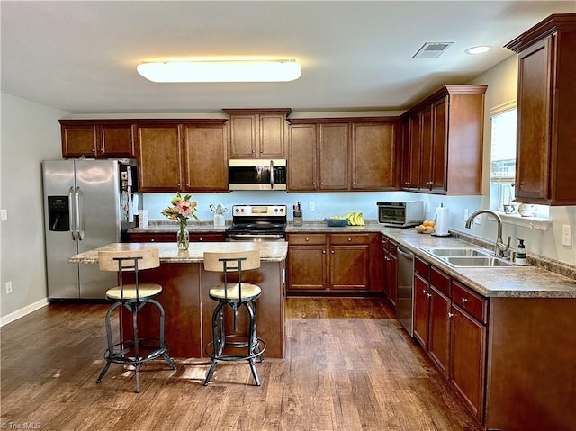 kitchen featuring appliances with stainless steel finishes, sink, a kitchen island, a kitchen breakfast bar, and dark hardwood / wood-style floors