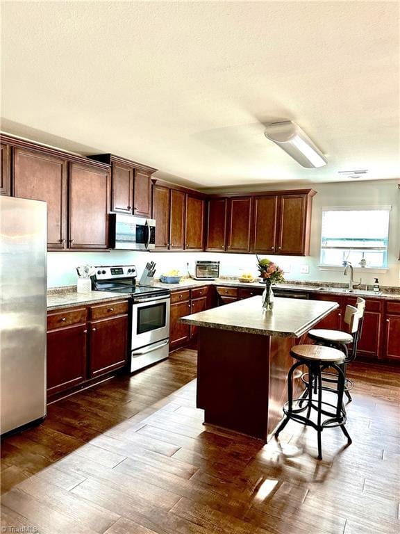 kitchen with sink, a kitchen breakfast bar, a kitchen island, stainless steel appliances, and dark wood-type flooring