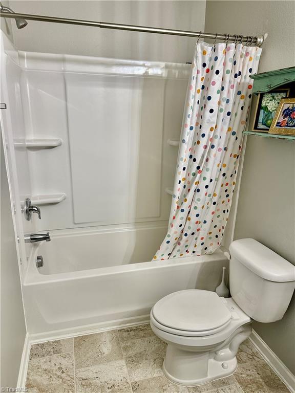 bathroom featuring shower / bathtub combination with curtain and toilet