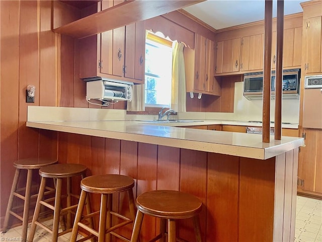 kitchen with a sink, stainless steel microwave, a breakfast bar area, light countertops, and light floors