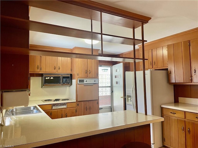 kitchen featuring white appliances, brown cabinetry, light countertops, and a peninsula