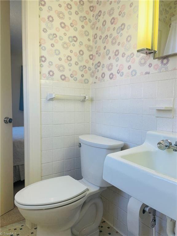 bathroom with a wainscoted wall, toilet, tile walls, and wallpapered walls