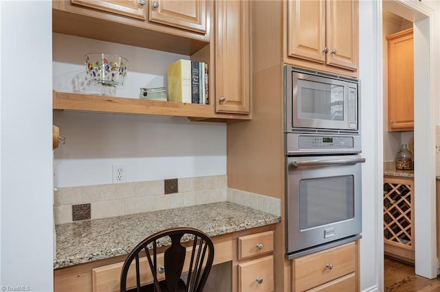 kitchen featuring light stone counters, light brown cabinetry, built in desk, and appliances with stainless steel finishes