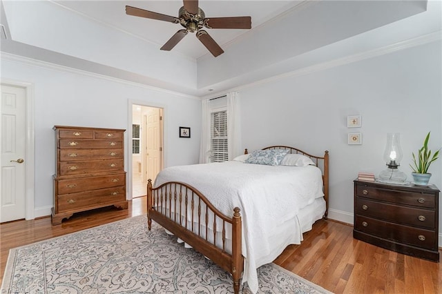 bedroom featuring crown molding, light hardwood / wood-style flooring, ensuite bath, ceiling fan, and a tray ceiling