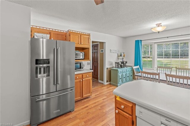 kitchen with a textured ceiling, light wood-type flooring, and appliances with stainless steel finishes