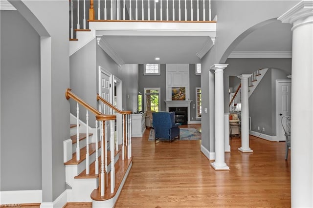 entryway featuring stairs, crown molding, light wood-style flooring, a fireplace, and arched walkways