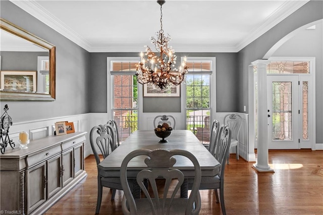 dining room featuring arched walkways, decorative columns, wood finished floors, a chandelier, and a wainscoted wall