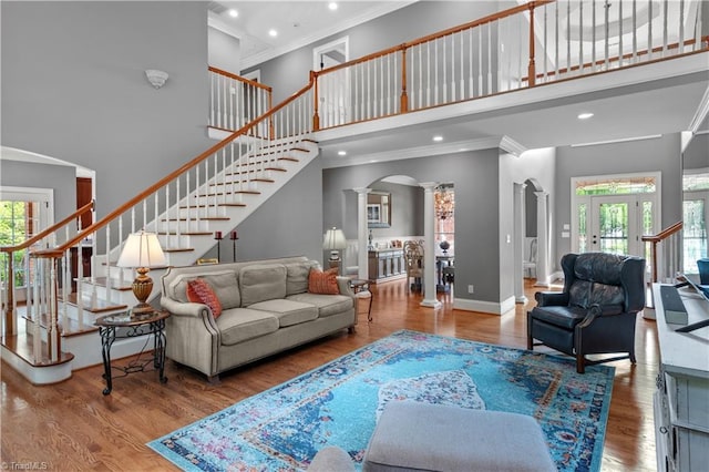 living area with decorative columns, a high ceiling, arched walkways, ornamental molding, and stairway