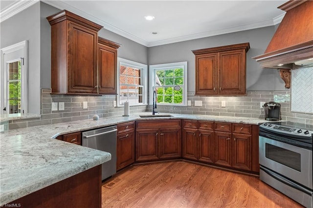 kitchen featuring appliances with stainless steel finishes, a sink, custom range hood, light wood-style floors, and light stone counters