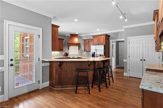 kitchen featuring stainless steel refrigerator with ice dispenser, backsplash, ornamental molding, a peninsula, and wood finished floors