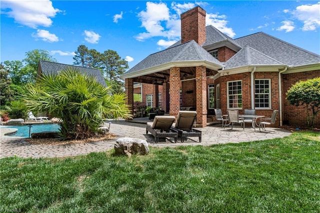 rear view of property with a chimney, brick siding, a patio, a yard, and a shingled roof
