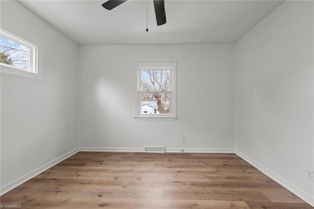 unfurnished room with a wealth of natural light, visible vents, baseboards, and wood finished floors