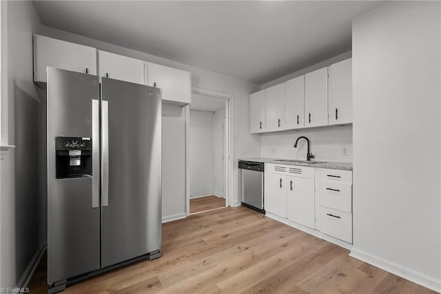 kitchen with tasteful backsplash, light wood-type flooring, stainless steel appliances, white cabinetry, and a sink