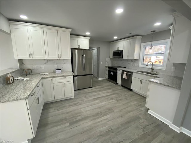 kitchen with sink, appliances with stainless steel finishes, hanging light fixtures, light stone counters, and white cabinets