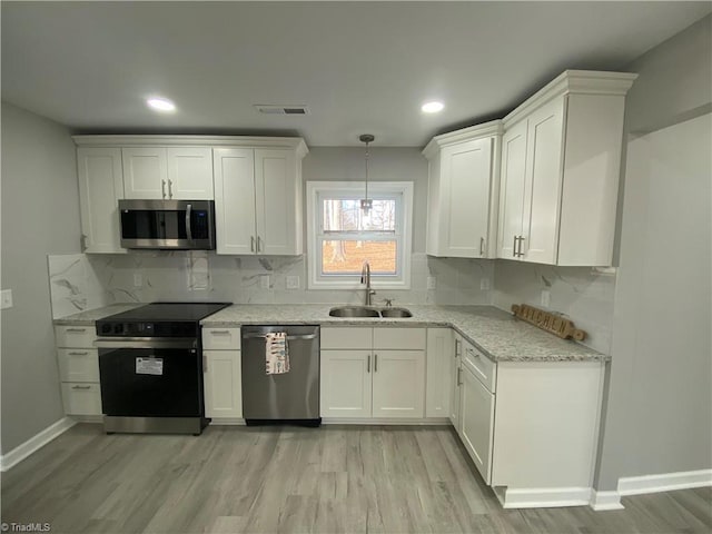 kitchen with sink, appliances with stainless steel finishes, light stone counters, light hardwood / wood-style floors, and white cabinets