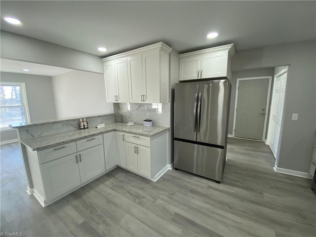 kitchen with stainless steel refrigerator, kitchen peninsula, light stone counters, and white cabinets