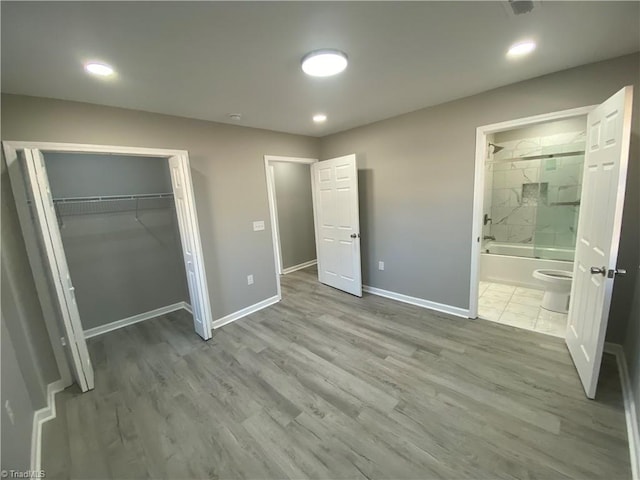 unfurnished bedroom with ensuite bath, light hardwood / wood-style floors, and a closet