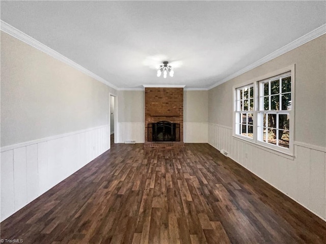 unfurnished living room with a brick fireplace, ornamental molding, dark wood-type flooring, and wainscoting