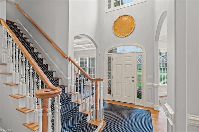 entrance foyer with a towering ceiling, beamed ceiling, coffered ceiling, and light hardwood / wood-style floors